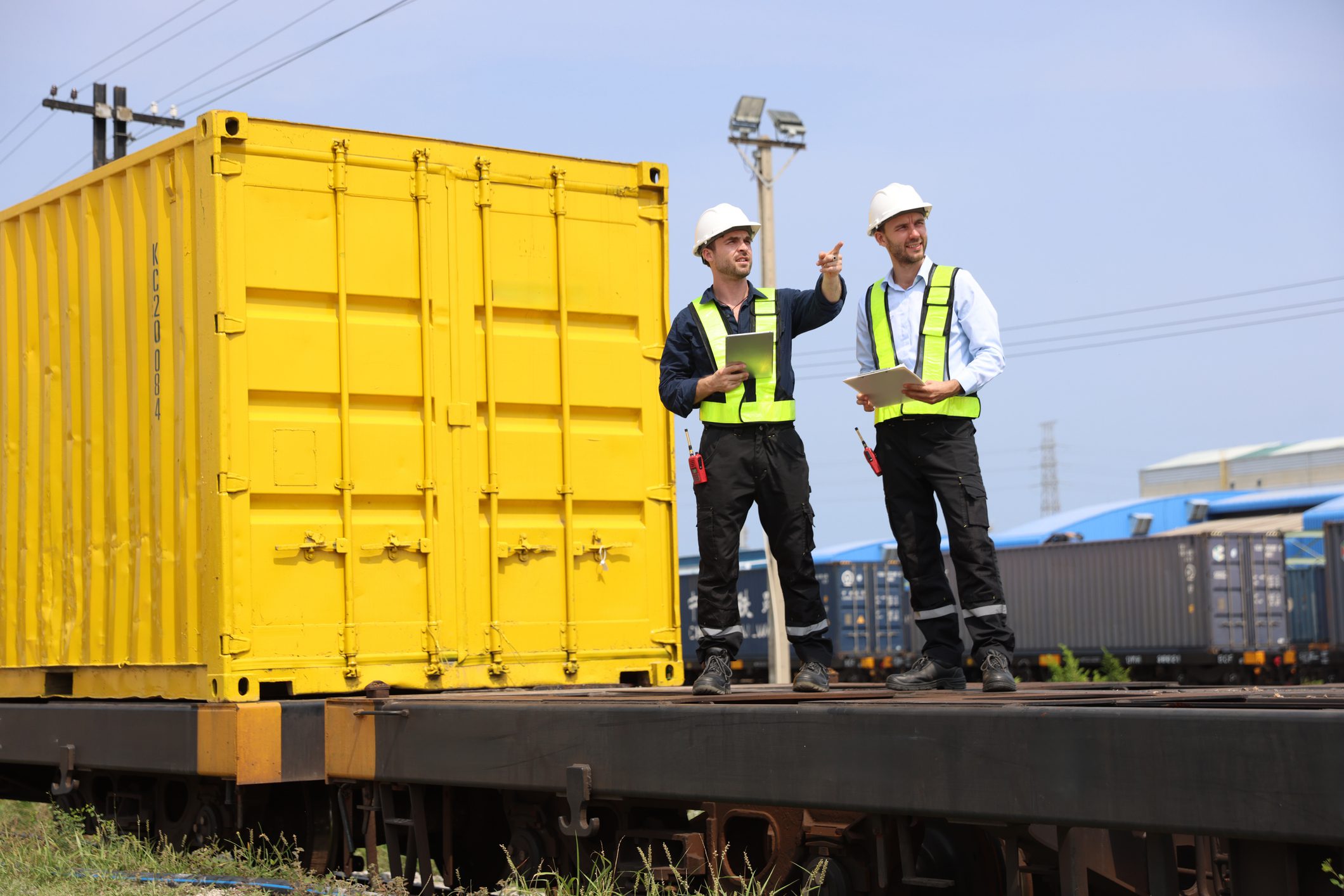 Two male logistics engineers are working at the Container railway yard. Cargo port storage for transportation and trading in the rail shipping yard