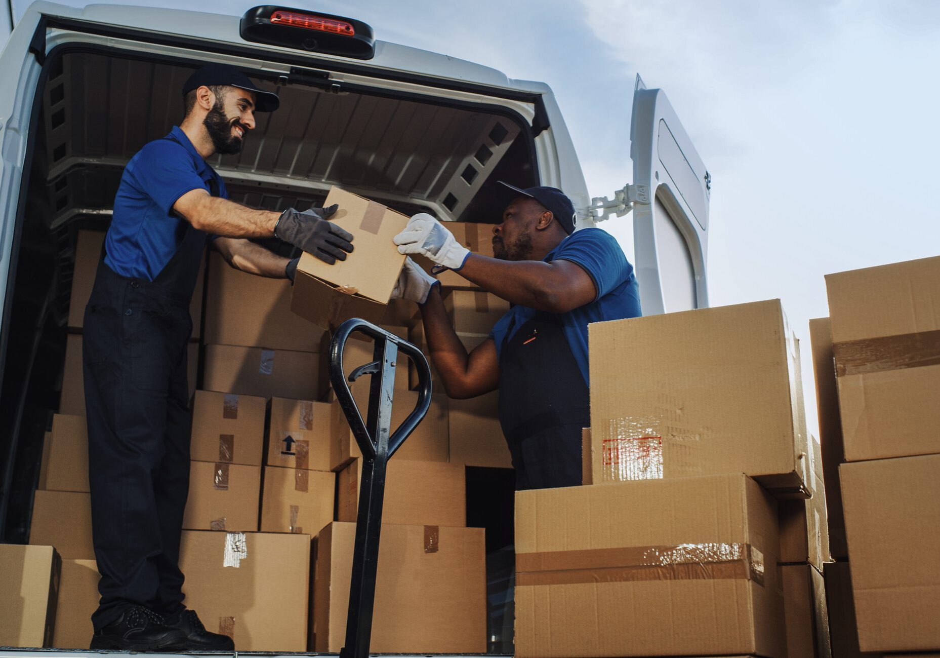 Logistics Warehouse Two Happy Workers Talk, Joke use Hand Pallet Truck Start Loading Delivery Truck with Cardboard Boxes, Online Orders, Purchases, E-Commerce Goods. Low Angle